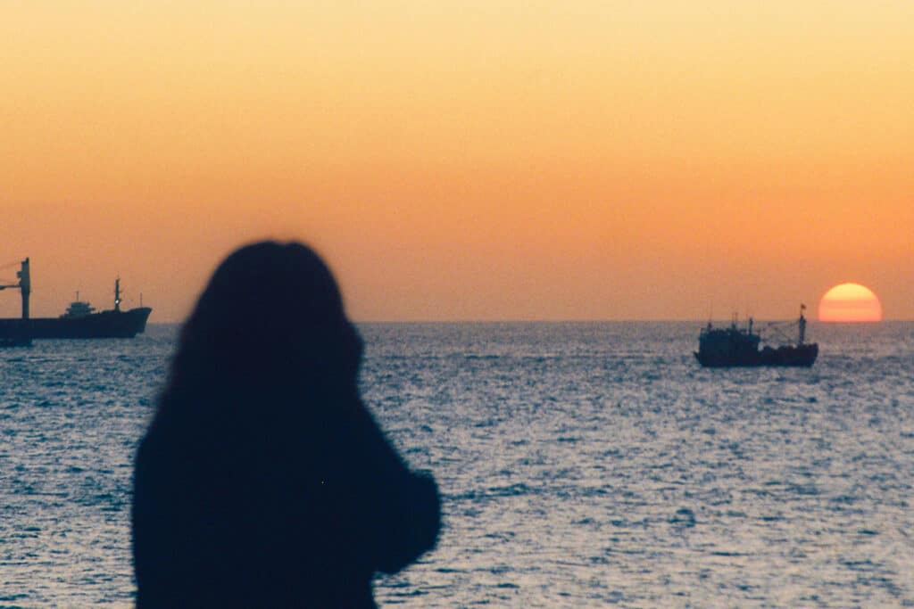 Vrouw kijkt naar schepen bij zonsondergang